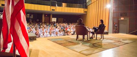 Two people sitting on a stage in chairs at a conference center